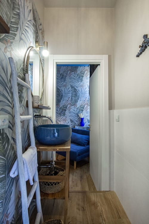 Bagno moderno presso la B&B Epimoni di Catania con lavabo azzurro, carta da parati tropicale e vista sulla città