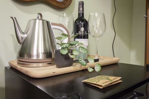 Vassoio benvenuto nella camera Alga di Epimoni B&B Catania: bollitore elettrico, bottiglia di vino, bicchieri, pianta e bustine di tè su legno