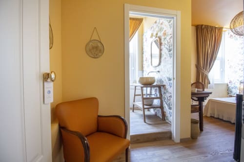 Luminosa camera gialla presso Epimoni B&B a Catania con poltrona arancione, vista sul bagno e tende dorate