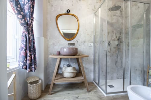 Lavabo del bagno presso Epimoni B&B Catania con mobile in legno, specchio rotondo, lavabo in ceramica viola e doccia a cascata