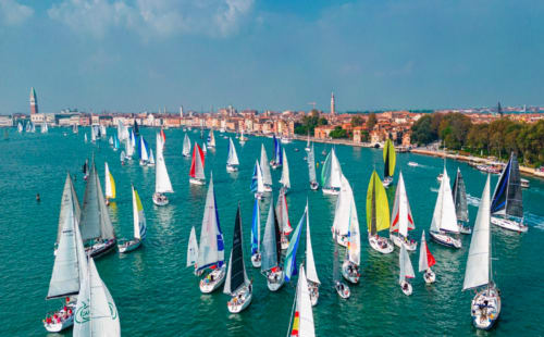 Regata di barche a vela sulla laguna turchese di Venezia con lo skyline della città e edifici storici sullo sfondo