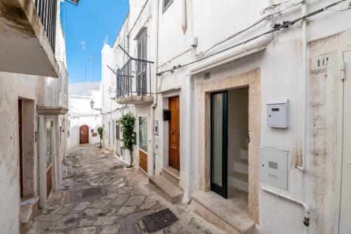 Vicolo imbiancato a calce a Ostuni con architettura tradizionale, cielo azzurro e porte in legno