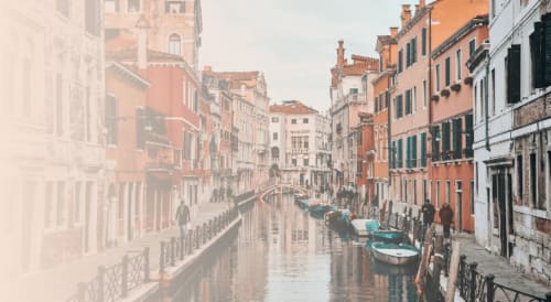 Canale veneziano con gondole turchesi, edifici storici in terracotta e ponti in pietra a Venezia