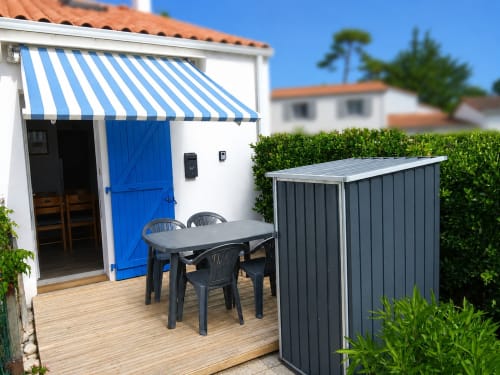 Terrasse de l'appartement Atlantique 165 aux Relais-Orbigny avec store rayé bleu, table à manger et vue sur le jardin