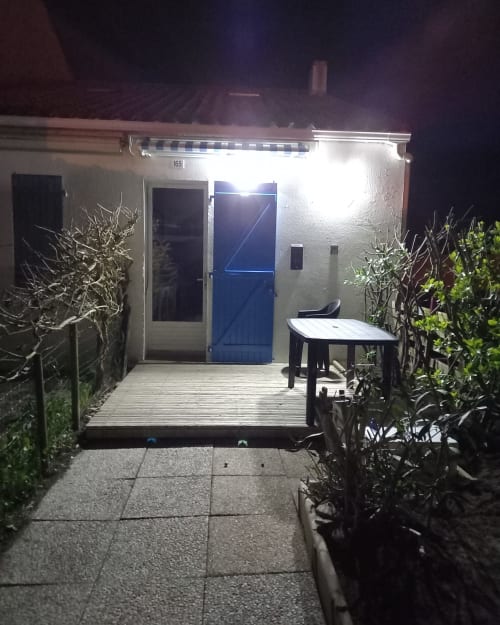 Vue nocturne de l'appartement Atlantique aux Relais-Orbigny avec entrée illuminée, terrasse en bois et coin détente jardin