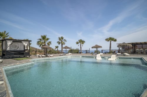 Piscina Paraje la Suerte en Adra con palmeras, tumbonas, vista al mar y sombrillas de terraza bajo cielo azul
