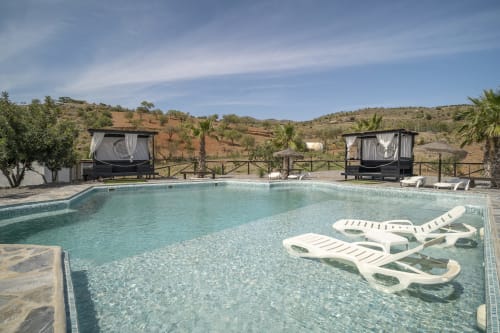 Piscina cristalina de la villa Cortijo La Suerte en Adra con tumbonas blancas, cabañas con dosel negro y vistas a la sierra