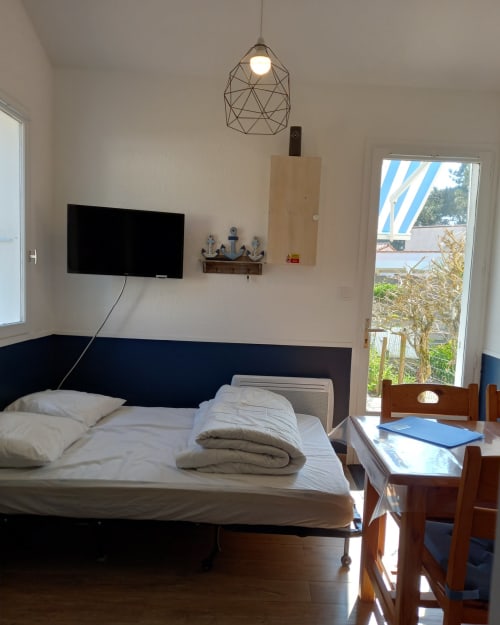 Chambre lumineuse aux Relais-Orbigny avec lit, TV écran plat, luminaire géométrique et accès à la terrasse et jardin