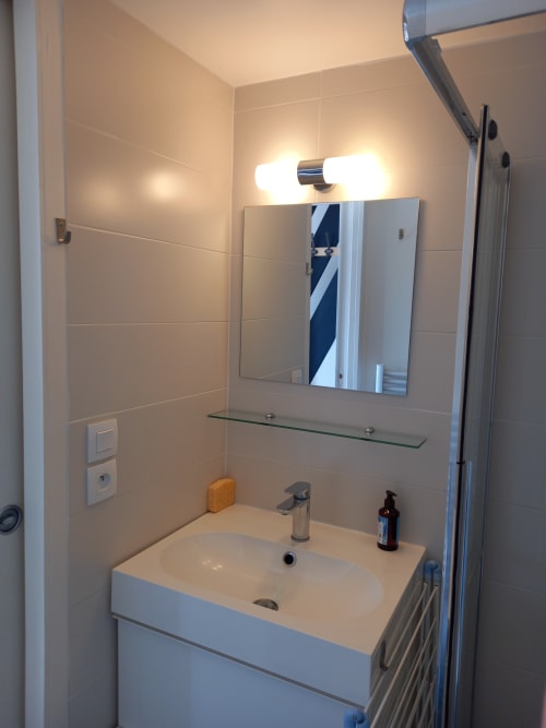 Salle de bain moderne de l'appartement Atlantique aux Relais-Orbigny avec vanité blanche, miroir, éclairage brillant et douche