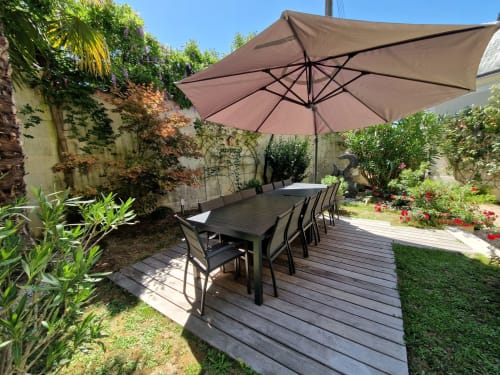 Dans la cour intérieure, espace de restauration extérieur avec table noire et chaises de jardin, parasol  