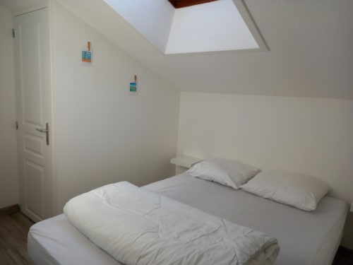 Chambre lumineuse sous les combles aux Relais-Orbigny avec literie blanche, lucarne et deux petits tableaux bleus