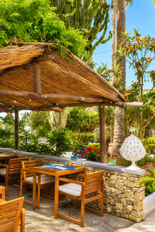 Terrazza ombreggiata con arredi in legno presso Villa Bina Sea Hotel a Serrara Fontana, con lussureggiante giardino tropicale sullo sfondo