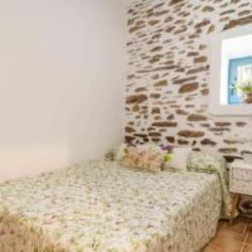 Dormitorio rústico de piedra en la villa Cortijo La Suerte en Adra con cama, paredes de ladrillo visto y ventana con vistas al jardín
