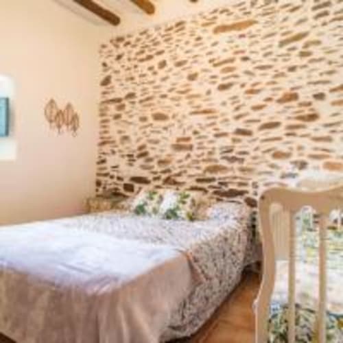 Dormitorio rústico con pared de piedra vista y ropa de cama blanca en la villa Cortijo La Suerte en Adra, España