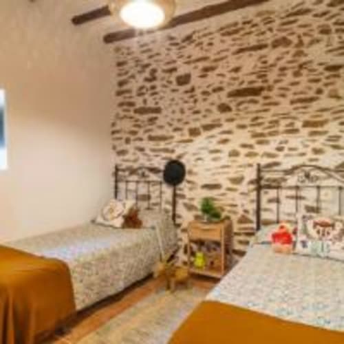 Dormitorio rústico en villa Cortijo La Suerte, Adra con paredes de piedra, camas gemelas con mantas naranjas, muebles de madera y techo