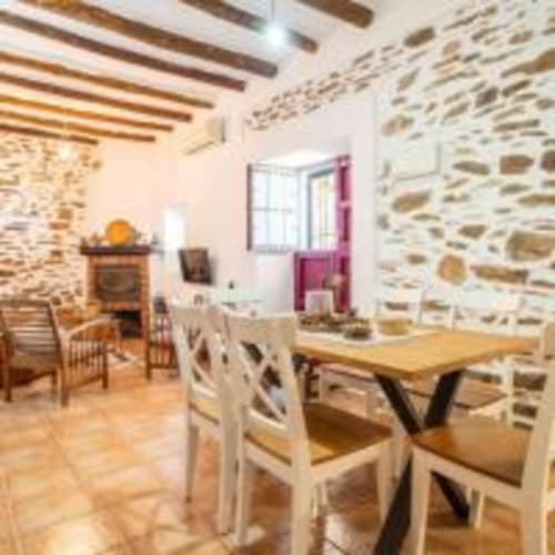 Comedor rústico con muros de piedra, vigas de madera, sillas blancas y mesa de madera en la villa Cortijo La Suerte en Adra