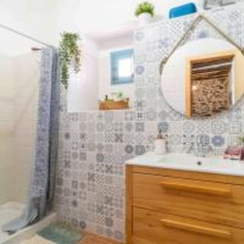 Baño moderno con paredes alicatadas, tocador de madera, plantas colgantes y acentos azules en la villa Cortijo La Suerte en Adra