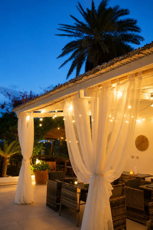 Elegante terrazza al tramonto del Villa Bina Sea Hotel con pergolato a tende bianche, sedute intrecciate e palme a Serrara