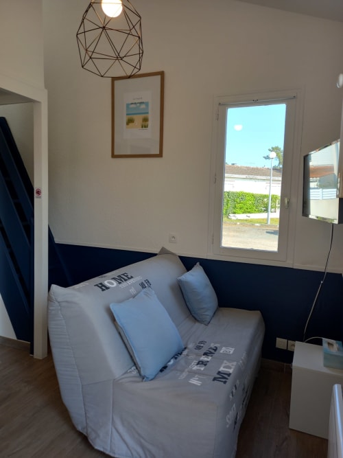 Salon moderne aux Relais-Orbigny : canapé gris, coussins bleus, luminaire suspendu géométrique et porte vitrée