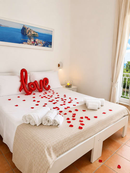 Camera romantica del Villa Bina Sea Hotel con palloncino rosso a forma di cuore, petali di rosa, asciugamani arrotolati e vista sul mare a Serrara