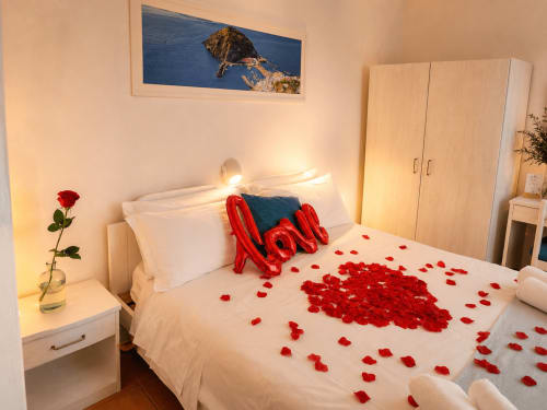Camera romantica Villa Bina Sea Hotel con petali di rosa rossa e palloncini rossi su biancheria bianca