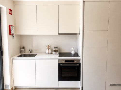 Cozinha moderna no estúdio Terra Clara, Esposende, com armários brancos, fogão preto e eletrodomésticos compactos