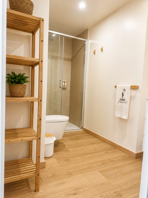 Casa de banho moderna com prateleiras em madeira, chuveiro e sanita branca no Terra Clara Studio em Esposende