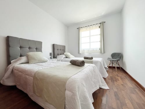Luminoso dormitorio doble en villa Casa Laferre, La Oliva, con cabeceros tapizados grises, ropa de cama blanca y suelos de madera