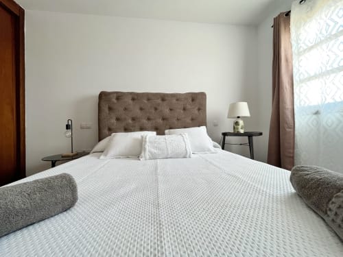 Dormitorio moderno en villa Casa Laferre, La Oliva, con cabecero capitonado, ropa de cama blanca y luz natural de ventana decorativa