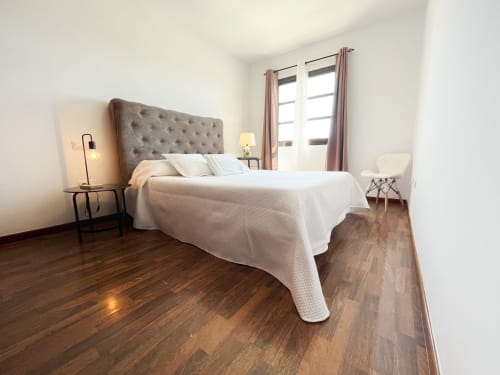 Dormitorio moderno en villa Casa Laferre, La Oliva, con cabecero capitoné, ropa de cama blanca, suelos de madera y luz natural