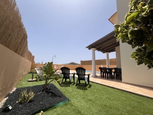 Terraza de la villa Casa Laferre en La Oliva con tumbonas negras, pérgola, césped impecable y vistas a la piscina