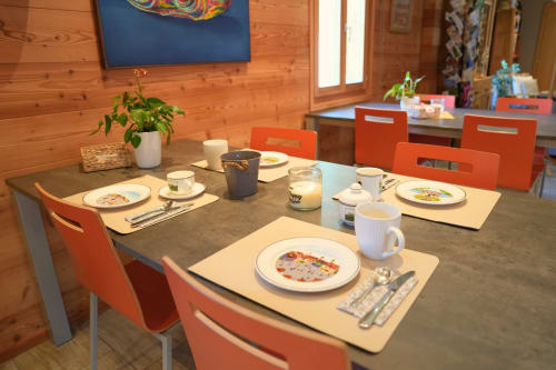 Salle à manger du gîte La Péniche à Evolène avec table dressée, chaises orange et murs en bois