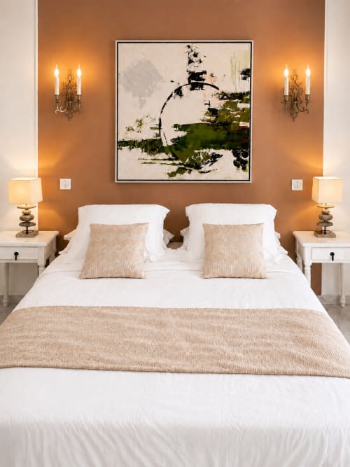 Elegantes Schlafzimmer einer Strandwohnung in Cannes mit warmen bernsteinfarbenen Wänden, weißer Bettwäsche und zeitgenössischem abstraktem Kunstwerk
