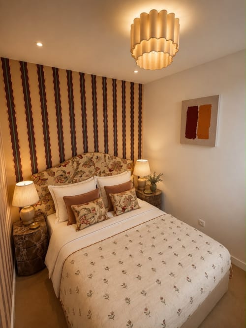 Chambre d'hôtel élégante à Deauville avec papier peint rayé, literie à motifs, lustre en laiton et éclairage chaleureux