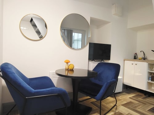 Modern Cork apartment lounge with blue armchairs, round mirrors, TV, and kitchen area at Cosy in Cork hotel.