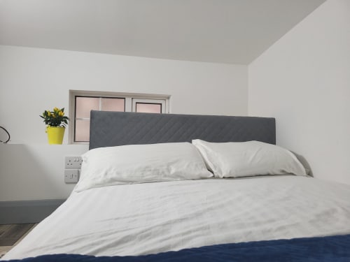 Modern bedroom in Historic Loft in Cork with gray upholstered headboard, white bedding, and yellow potted plant on nightstand