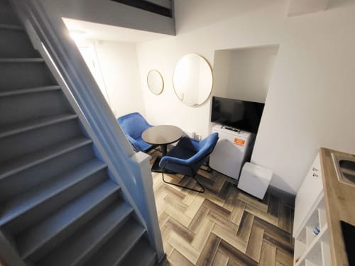 Compact loft studio with blue chair, round mirrors, TV, minibar, and herringbone flooring at Cosy in Cork apartment, Cork