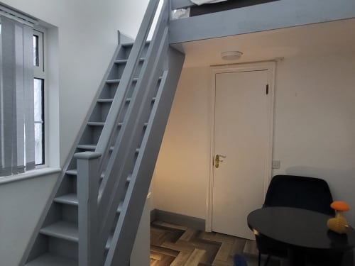Historic loft apartment in Cork featuring gray staircase with shelving, white door, round black table, and wooden flooring