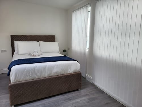 Modern studio bedroom at Cosy in Cork with brown upholstered bed, white bedding, blue throw, and vertical blinds