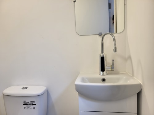 Compact bathroom at Cosy in Cork studio apartment with white toilet, curved sink, chrome faucet and mirror