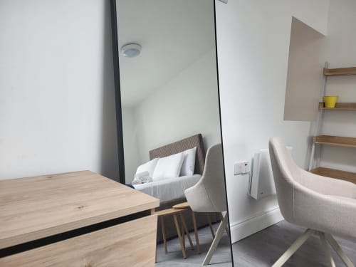 Cosy Studio in Cork showing wooden desk, beige chair, and bed with white pillows in modern apartment
