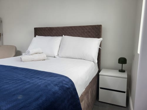 Modern studio bedroom in Cork with brown upholstered headboard, white bedding, blue throw, and white nightstand with green