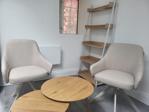 Modern studio seating area with two beige chairs and round wood table in Cork historic apartment
