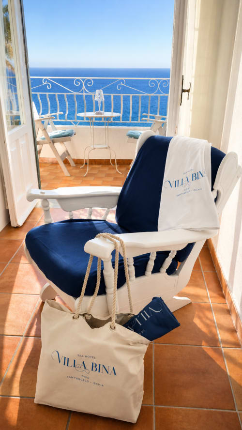 Balcone del Villa Bina Sea Hotel con sedia blu e bianca, asciugamano e vista sul Mar Mediterraneo da Ischia