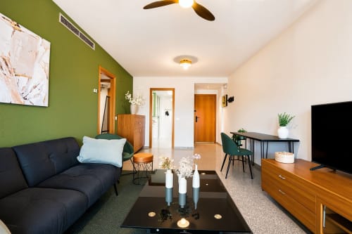 Salon moderne d'appartement à Valence avec mur accent vert, canapé noir, téléviseur et salle à manger près de la plage