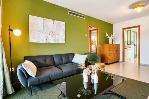 Salon moderne avec murs vert citron, canapé sombre, meubles en bois et fleurs blanches sur table noire