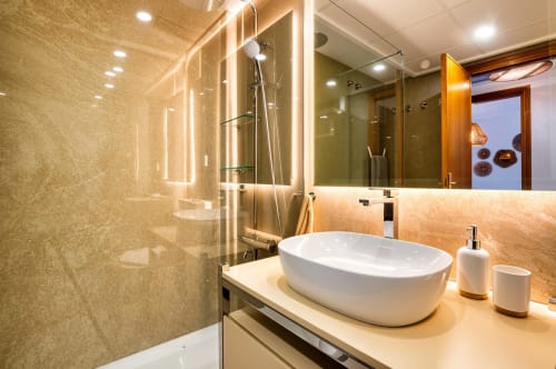 Salle de bain moderne avec lavabo ovale blanc, miroir éclairé, douche à l'italienne et carrelage en marbre beige chaud à Valence