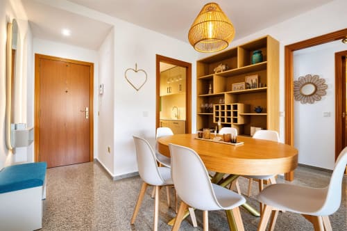 Salle à manger moderne avec table en bois, chaises blanches et étagères intégrées dans un appartement en bord de mer à Valence