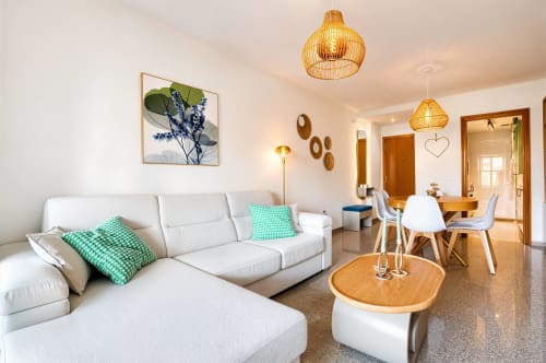 Salon moderne en bord de mer avec canapé blanc, accents bois, coussins turquoise et coin repas chez Pataconablue