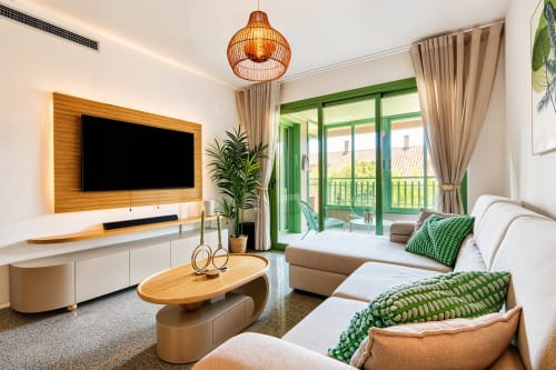 Salon moderne avec TV, canapé beige, table basse en bois, portes-fenêtres vertes et vue sur la mer à Pataconablue Valencia
